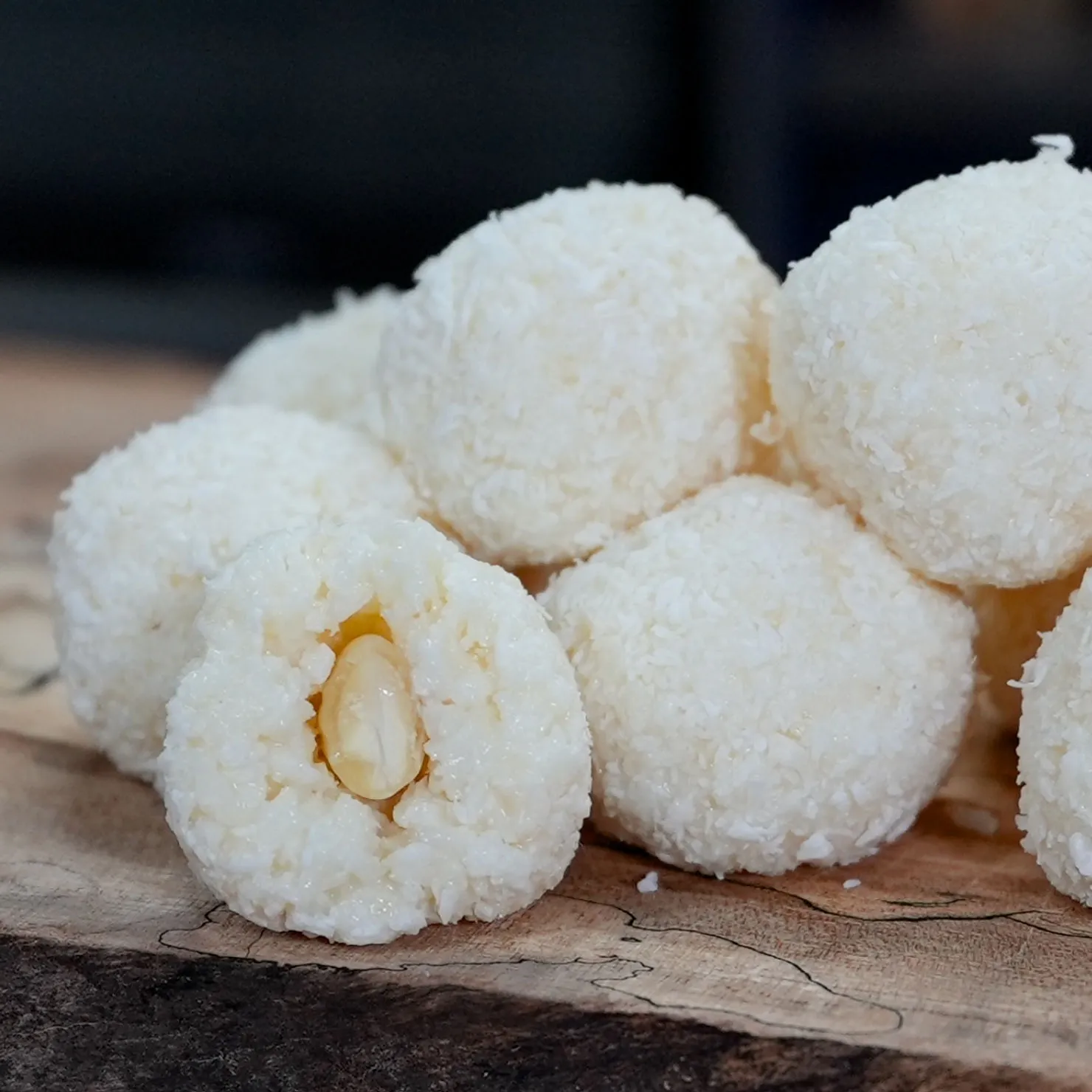 Coconut-covered confections with almond centers on a wooden board. The treats are round and white, evoking a sweet and cozy mood.