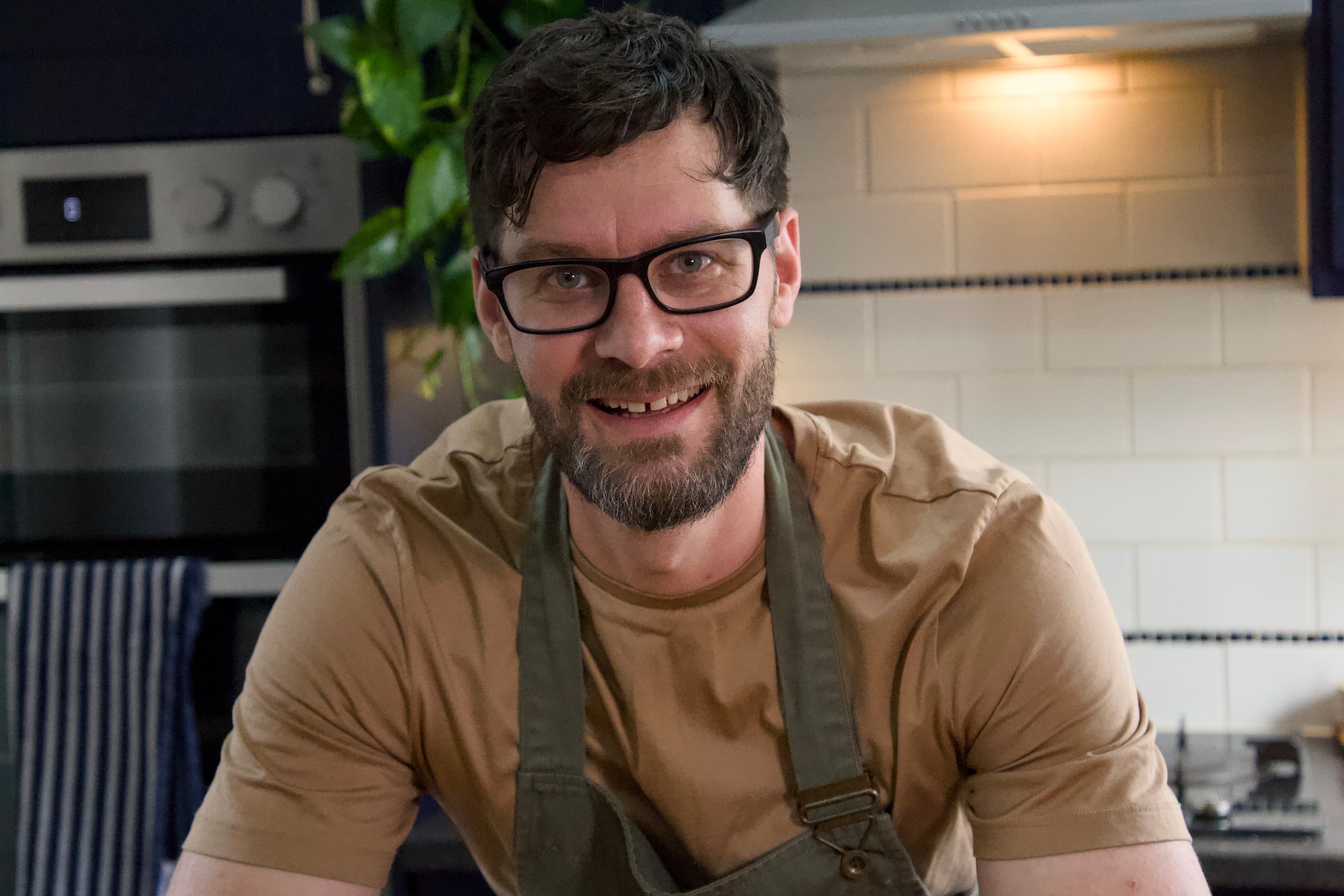 Tom leaning on a wooden worktop behind a pile of squash, potatoes and red onions