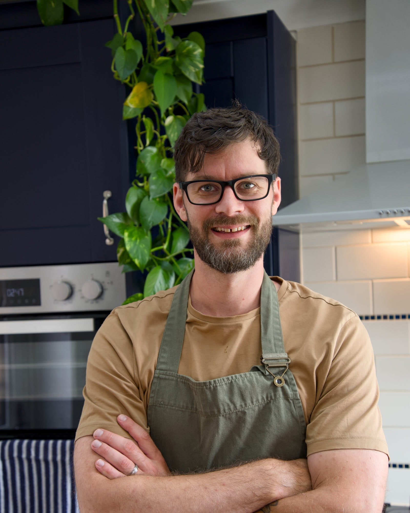 Tom standing in his kitchen in an apron, arms folded, looking at the camera