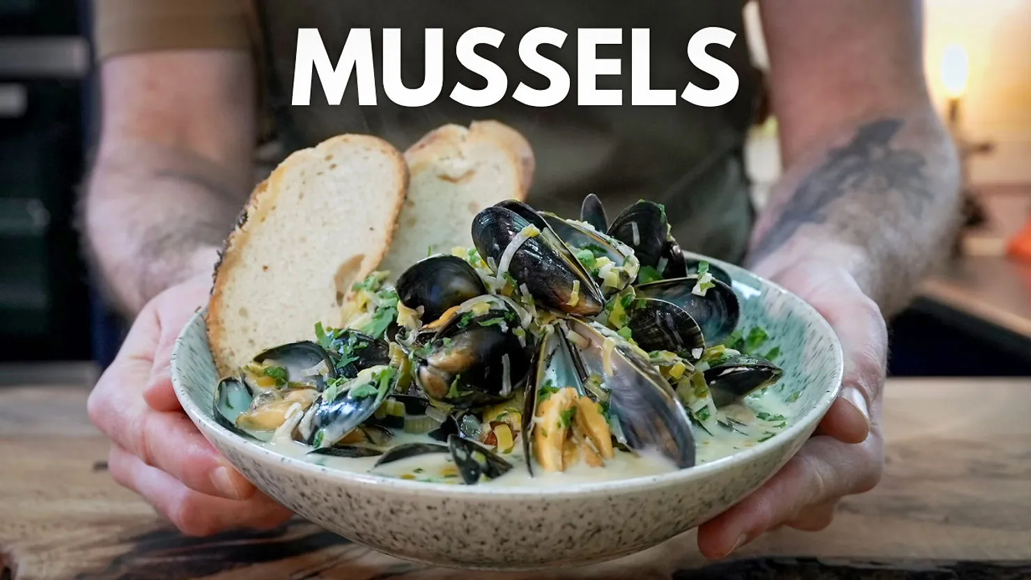 Person holding a bowl of mussels in creamy sauce with bread slices, text "MUSSELS" above. Rustic table setting. Mood: inviting.